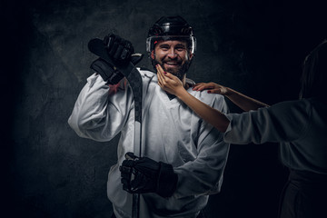 Happy brutal hockey player is posing for photographer while woman with accurate manicure is touching him.