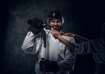 Portrait of middle aged hockey player with woman's hand on his beard.