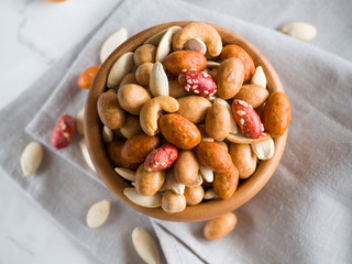 Crispy assorted mixed nuts with different flavors and pumpkin seeds in the wooden bowl and grey linen towel as background. Roasted nuts coated by salt and spicy. Snack for beer. Close up. Top view.