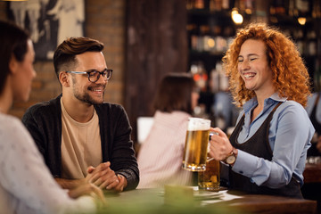 Happy waitress serving beer to a couple in a pub.
