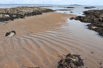 Coastline at low tide with exposed rocks and ripples in the sand