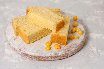 Freshly baked corn bread on a round wooden white board with corn on a light background.