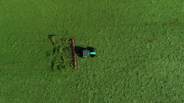 Aerial top-down view of green grass farm field with tractor raking grass so grass can dry faster and becomes dried grass or hay then be picked up and kept for cattle fodder for winter food 4k quality