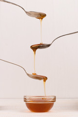 Liquid May honey flows down into spoons in a jar. Sweet cascade on a white background.