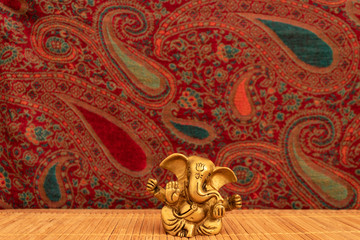 Fototapeta na wymiar Golden ganesha figure on bamboo mat with oriental paisley pattern textile background. Yoga concept