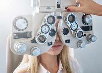 Optometry concept - pretty young woman having her eyes examined by eye doctor. - Powered by Adobe
