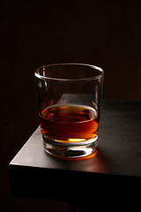 A glass of whiskey without ice on a wooden table. Low key. Vertical orientation.