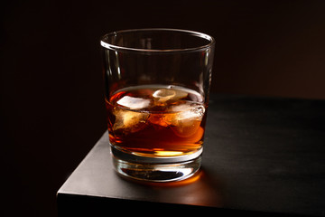 A glass of whiskey with ice on a wooden table. Low key. Horizontal orientation. 