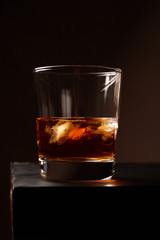 A glass of whiskey with ice on a wooden table. Low key. Vertical orientation.