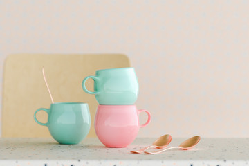 3D rendering illustration of pastel cups and copper spoons on a terrazzo table with chair in background