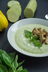 Cream soup of mashed potatoes with zucchini and basil and crackers on a dark background.