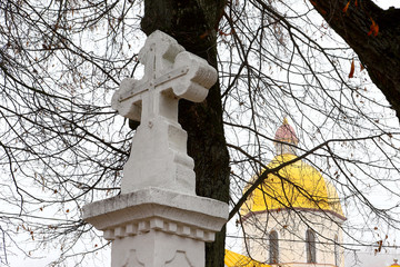 Old Weathered Stone Tomb Cross, Background of New Orthodox Church and Old Trees in Fog. Autumn.