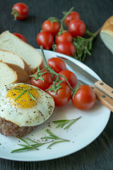 Beef steak with fried egg in spices served on a white plate. American dish. Dark wooden background. Side view. Close-up.