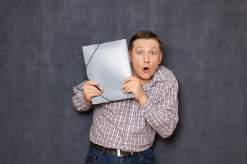 Portrait of surprised shocked man looking from behind folder