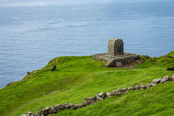 View on the Mykines island with moody clouds covering the top of the mountains and sheep grazing on the pasture, Mykines island, Faroe Islands, Europe.