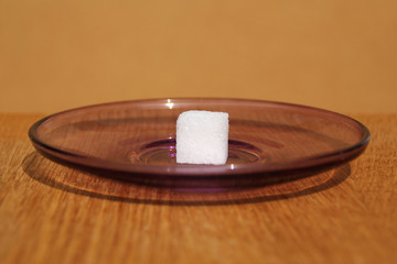 Obraz premium one white sugar cube on a plate, concept of excess sugar intake, diabetic, close-up, copy space