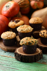 Homemade healthy pastry concept. Yummy imperfect pumpkin muffins with seeds and chocolate with winter squashes on wood slabs on shabby green background copy space