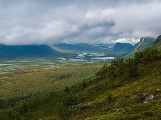 View on meandering river delta at Rapadalen valley in Sarek national park, Sweden. Lapland mountains, rocks and birch trees. Early autumn colors, moody sky with clouds.