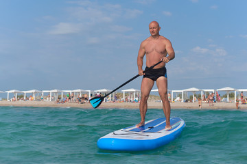 A sporty man with a paddle floats on a SAP Board on the sea