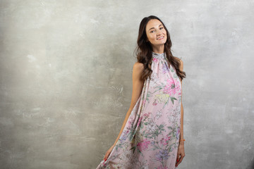 Portrait of an attractive young woman in a summer pink dress on a gray background