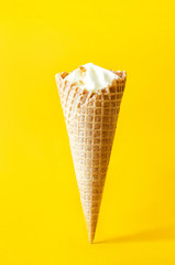 A creamy ice cream in a horn is standing on a yellow background. Delicious cream ice cream.