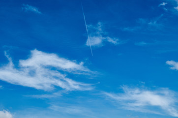 Trace of an airplane in the sky. Bright sky with white clouds.