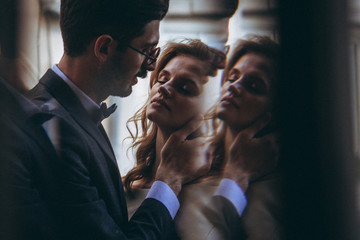 stylish wedding couple of pretty bearded groom and elegant blonde woman in wedding dress posing for photo in chic palace, copy space, noise effect