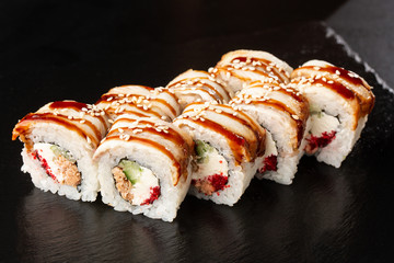Golden dragon sushi roll. Sushi Rolls with flying fish caviar , tuna, eel, cucumber, sesame seeds and Cream Cheese inside and on black slate isolated. Horizontal