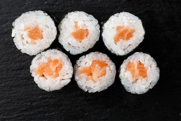 Maki Sushi Rolls with salmon on black stone on dark background. Sushi menu. Japanese food. Closeup of delicious japanese food with sushi roll. Horizontal photo
