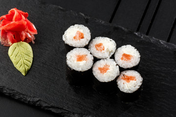 Maki Sushi Rolls with salmon on black stone on dark background. With ginger and wasabi. Sushi menu. Japanese food. Closeup of delicious japanese food with sushi roll. Horizontal photo