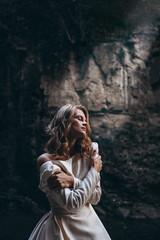Fototapeta premium gentle and graceful portrait of a pretty bride dressed in a white dress with a bare back and shoulders posing for a photo by the waterfall