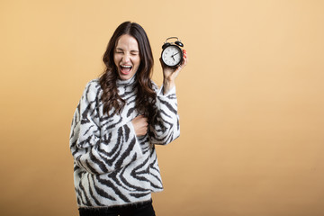 Fototapeta premium Image of a young beautiful woman posing isolated against an orange wall holding an alarm clock