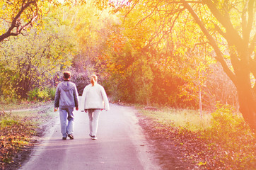 Two people, man and woman walking in autumn park with yellow, red and orange trees, falling leaves...