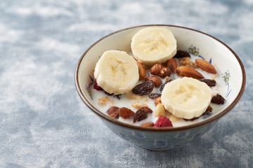 Bowl of granola with milk, nuts, raisins and banana. Concept for a tasty and healthy meal. Rustic wooden background. Close up.