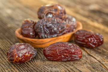 Juicy dates in a bowl on a old wooden table .