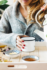 A female model is drinking herbal tea with honey for flu, she is pouring herbal tea and honey into a white enamel cup