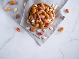 Crispy assorted mixed nuts with different flavors and pumpkin seeds in the wooden bowl and grey linen towel as background. Roasted nuts coated by salt and spicy. Snack for beer. Close up. Top view.