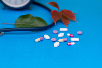 Alarm clock for the timely adoption of pills, a stethoscope, multi-colored pills, on a blue background.