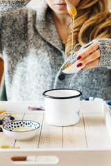 A female model is drinking herbal tea with honey for flu, she is pouring herbal tea and honey into a white enamel cup