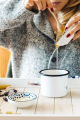 A female model is drinking herbal tea with honey for flu, she is pouring herbal tea and honey into a white enamel cup