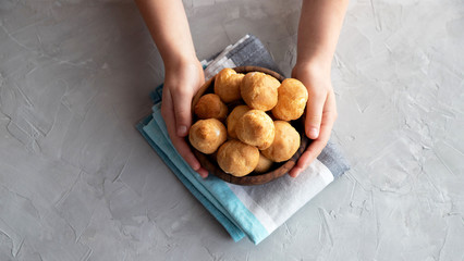 A small wooden bowl full of homemade eclairs in hands on a dining napkin on a gray concrete table