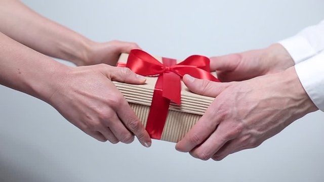 Female and male hands give a box with a gift. Holiday packaging.