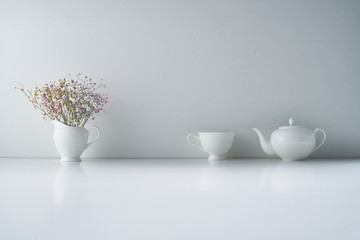 Composition with white porcelain tea-ware on a light gray background with a delicate bouquet of...