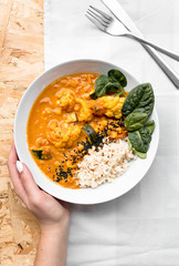 Curry z kalafiora w białej misce trzymane dłonią ze sztućcami