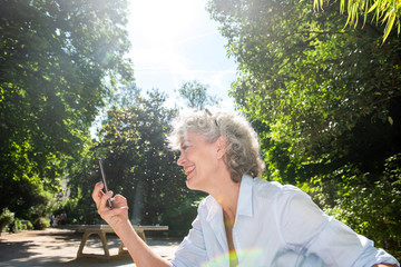 Close up portrait of smiling older woman looking at mobile phone ion park