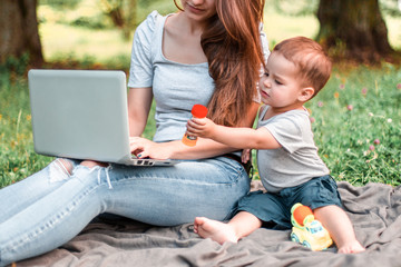 Mother with son sitting in the park and work on laptop.