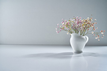 Composition with white porcelain tea-ware on a light gray background with a delicate bouquet of flowers