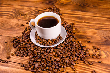Cup of hot coffee and scattered coffee beans on wooden table