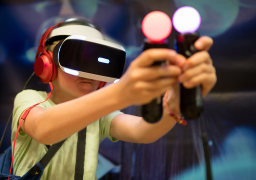 Young teenager boy using a Virtual reality headset with goggles and hands motion controllers in playing game zone. Modern technologies concept image.