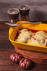 Delicious Chicken Parmigiana served in yellow baking dish with on a wooden table and stone or concrete background..